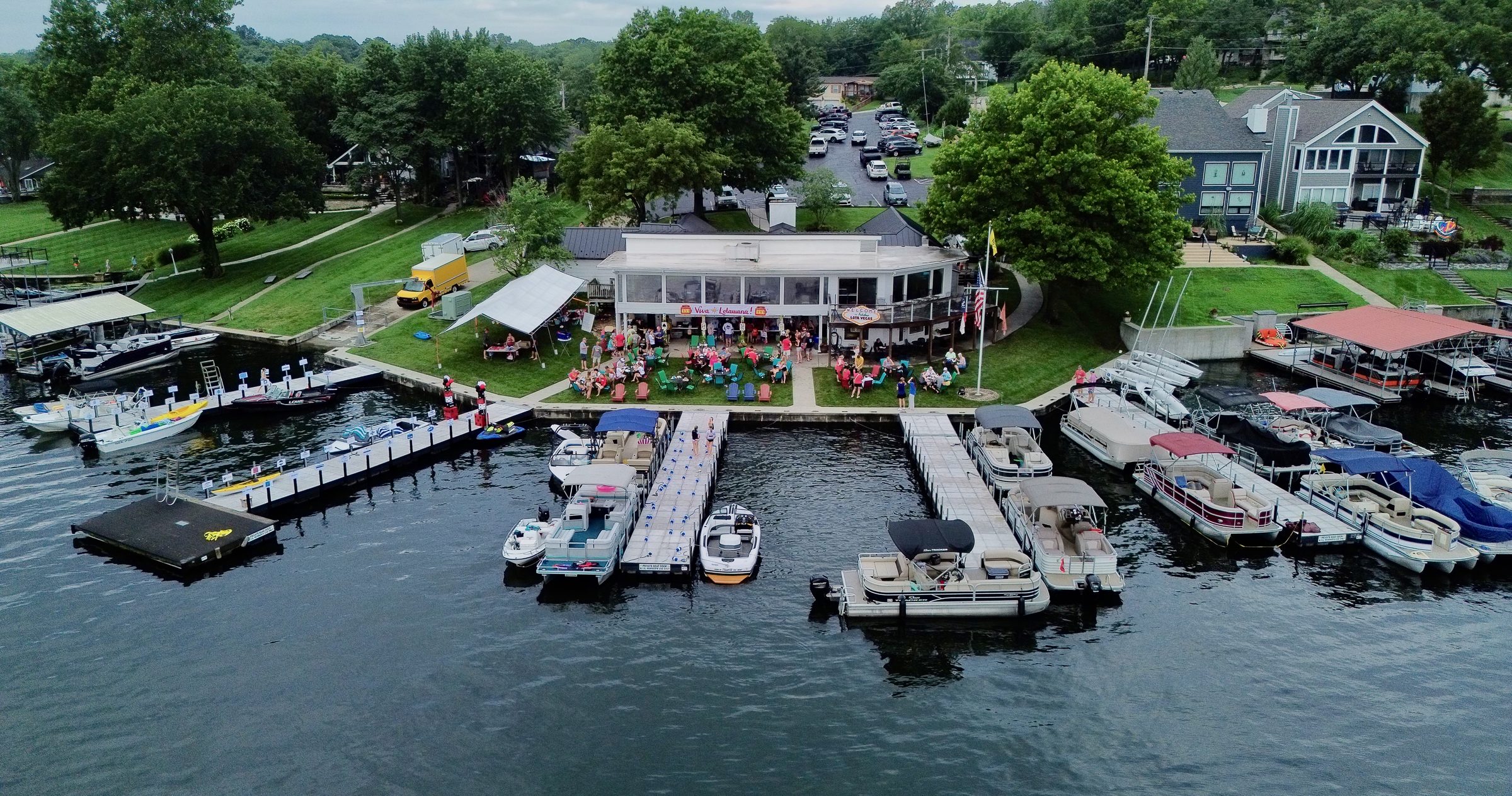 Aerial view of the Lake Lotawana marina and clubhouse, with docks, pontoon boats, and lakefront homes lining the cove